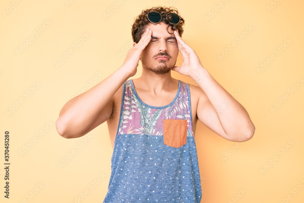Young caucasian man with curly hair wearing casual style with sleeveless shirt with hand on head, headache because stress. suffering migraine. Young caucasian man with curly hair wearing casual style with sleeveless shirt with hand on head, headache because stress. suffering migraine.