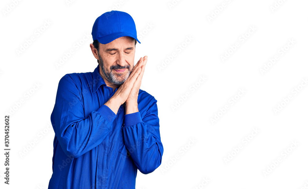 Middle age handsome man wearing mechanic uniform sleeping tired dreaming and posing with hands together while smiling with closed eyes. Middle age handsome man wearing mechanic uniform sleeping tired dreaming and posing with hands together while smiling with closed eyes.