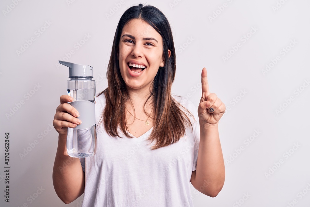 Young beautiful brunette woman drinking bottle of water over isolated white background smiling with an idea or question pointing finger with happy face, number one Young beautiful brunette woman drinking bottle of water over isolated white background smiling with an idea or question pointing finger with happy face, number one