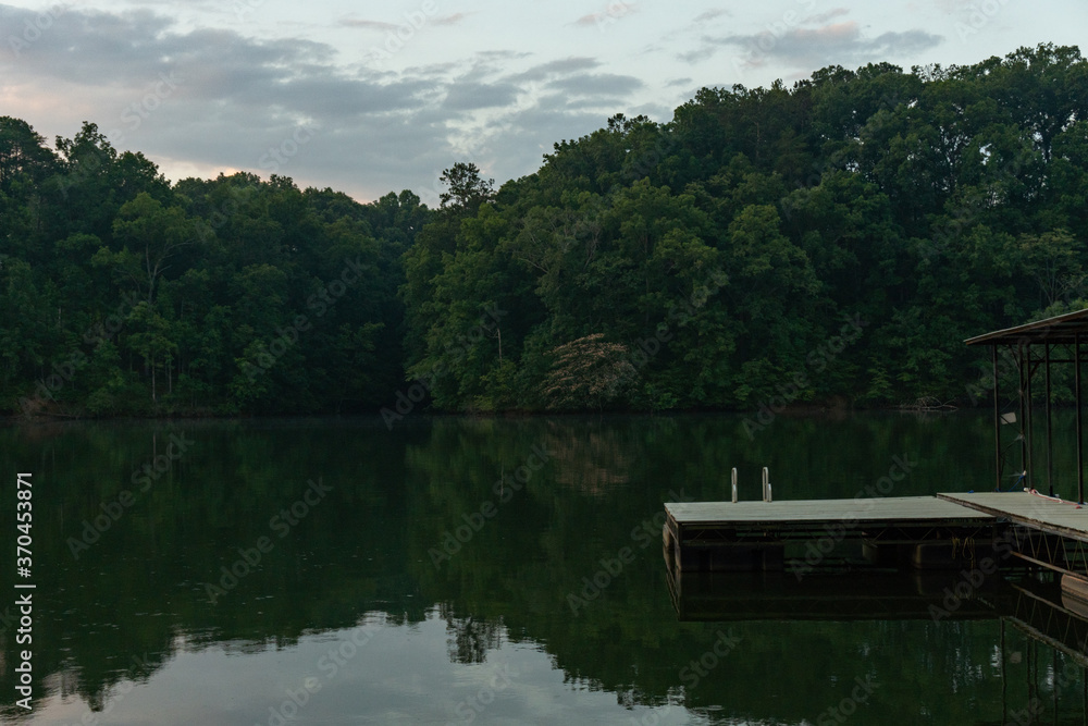 The swim platform on a dock at dawn with a ladder leading into the water surrounded by trees and their reflection in the water