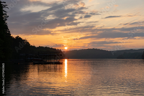 The sun rises over Lake Lanier in Georgia, showing a reflection on the water under an orange cloudy sky © Liz W Grogan