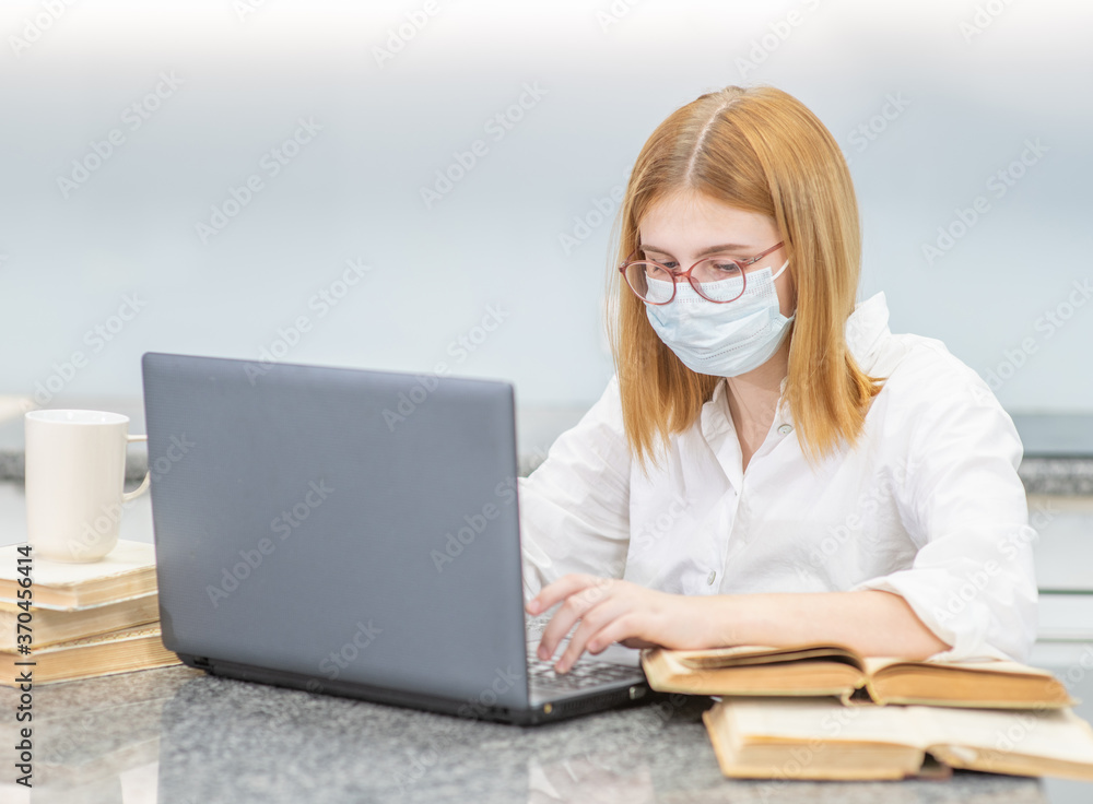 Young girl wearing medical mask is engaged in distance learning with a laptop. Quarantine and coronavirus epidemic concept Young girl wearing medical mask is engaged in distance learning with a laptop. Quarantine and coronavirus epidemic concept