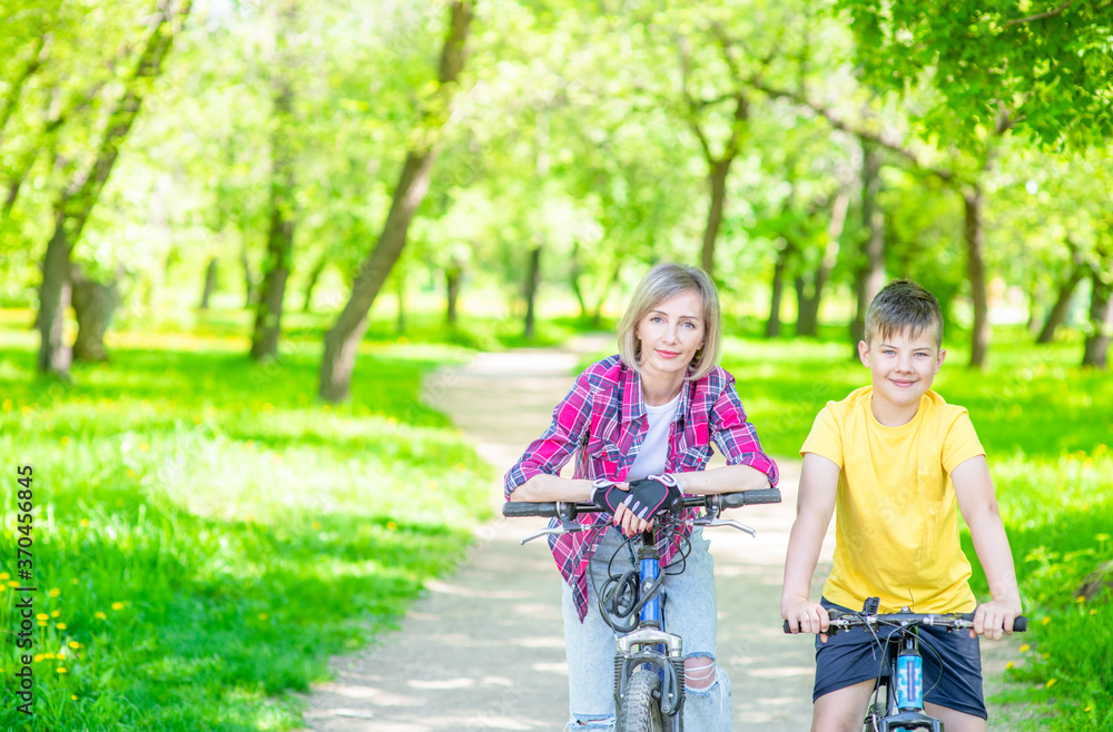 Portrait of a mother and son standing with bicycles in sunny summer park. Empty space for text Portrait of a mother and son standing with bicycles in sunny summer park. Empty space for text