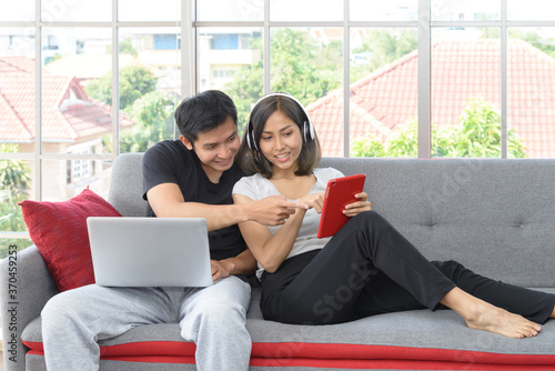 Young asian couple wear casual clothing relaxing sitting on cozy couch in living room working with computer laptop and tablet PC at home. Love, happiness, work at home concept