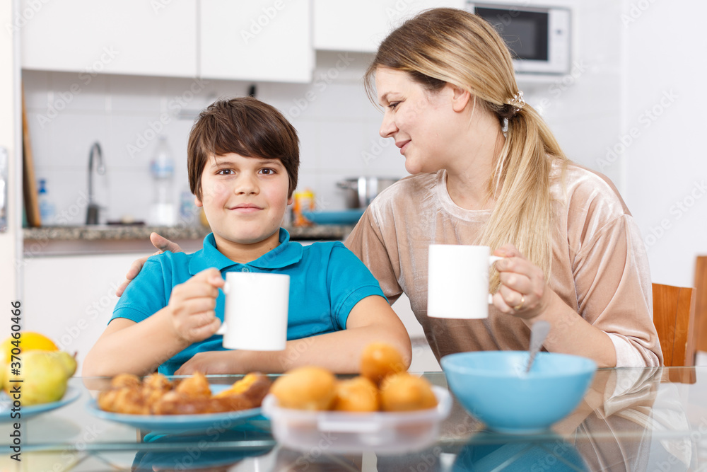 Young woman with tween son enjoying meal at kitchen table
