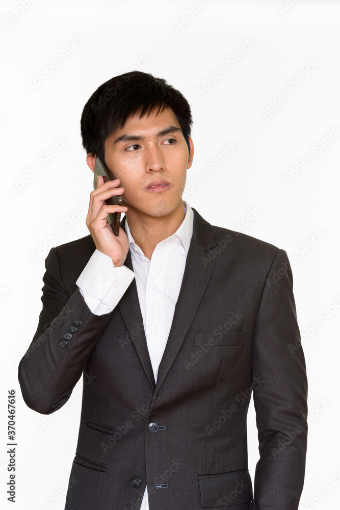 Studio shot of young handsome Asian businessman talking on mobile phone isolated against white background Studio shot of young handsome Asian businessman talking on mobile phone isolated against white background