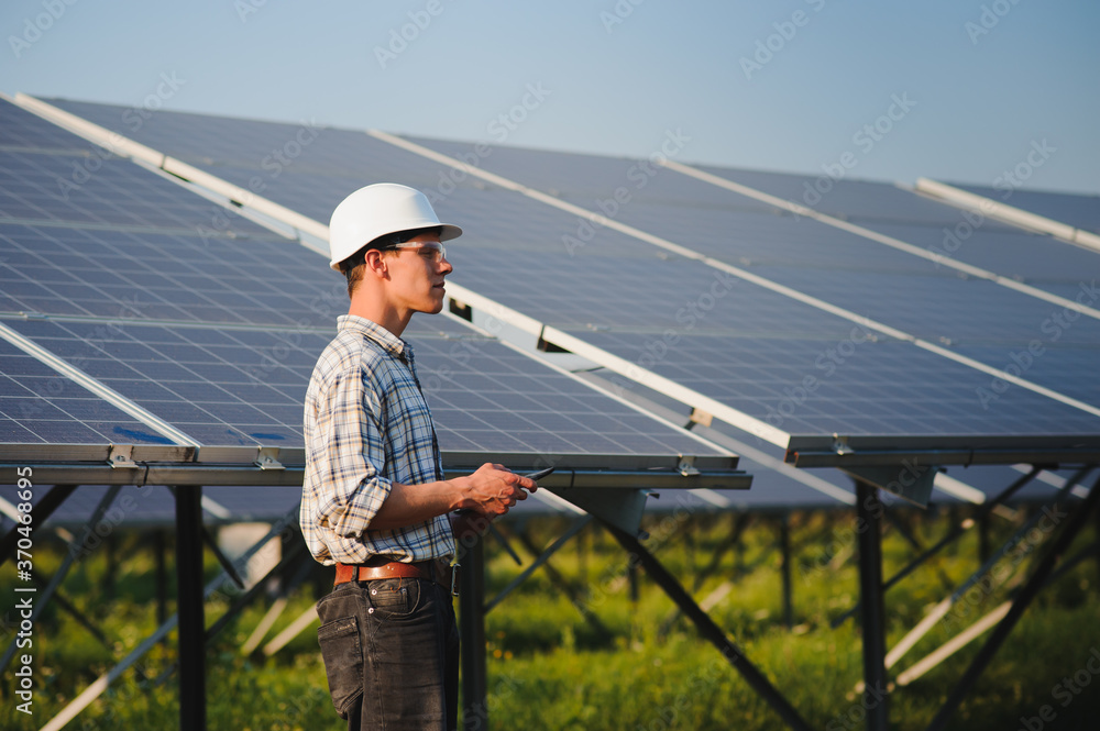 Male worker solar power plant with a tablet on a background of photovoltaic panels.