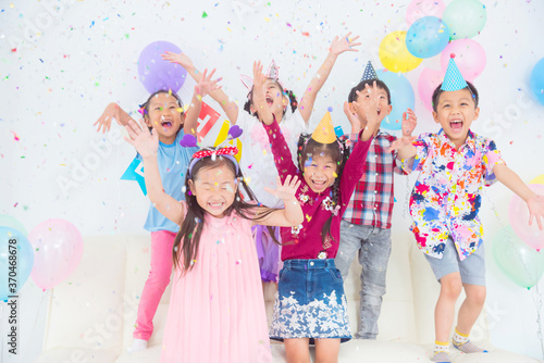 Group of Happy Asian Kids Raise Hands Up and Enjoy Throwing Colorful Confetti with Friends in Birthday Party.