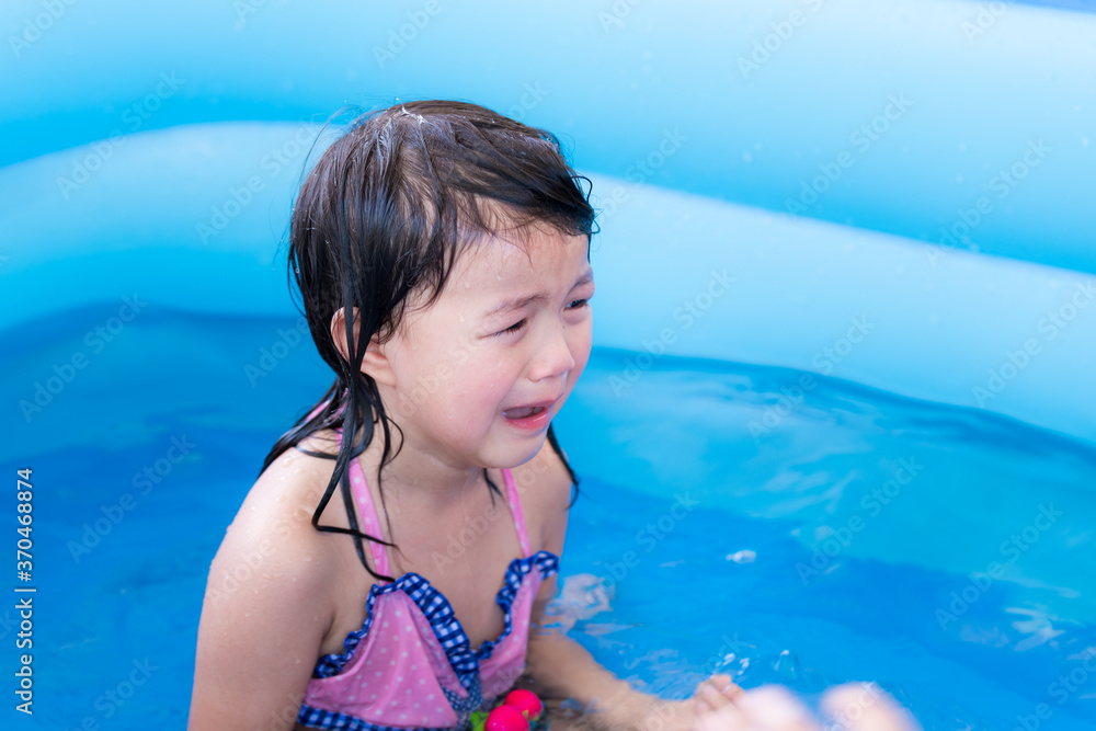 Selective focus, Asian girl crying in blue rubber pool. She cried from being teased by her friend while playing in the water. Children suffer pain from leisure activities. Children are 5 years old.