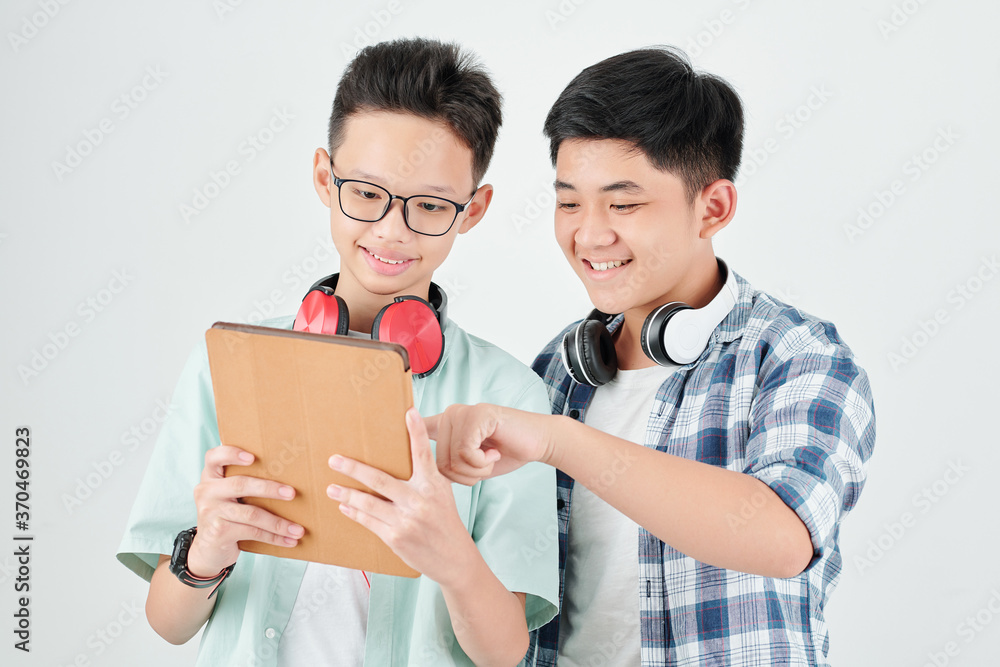 Excited Asian teenage boys discussing new application on tablet computer Excited Asian teenage boys discussing new application on tablet computer