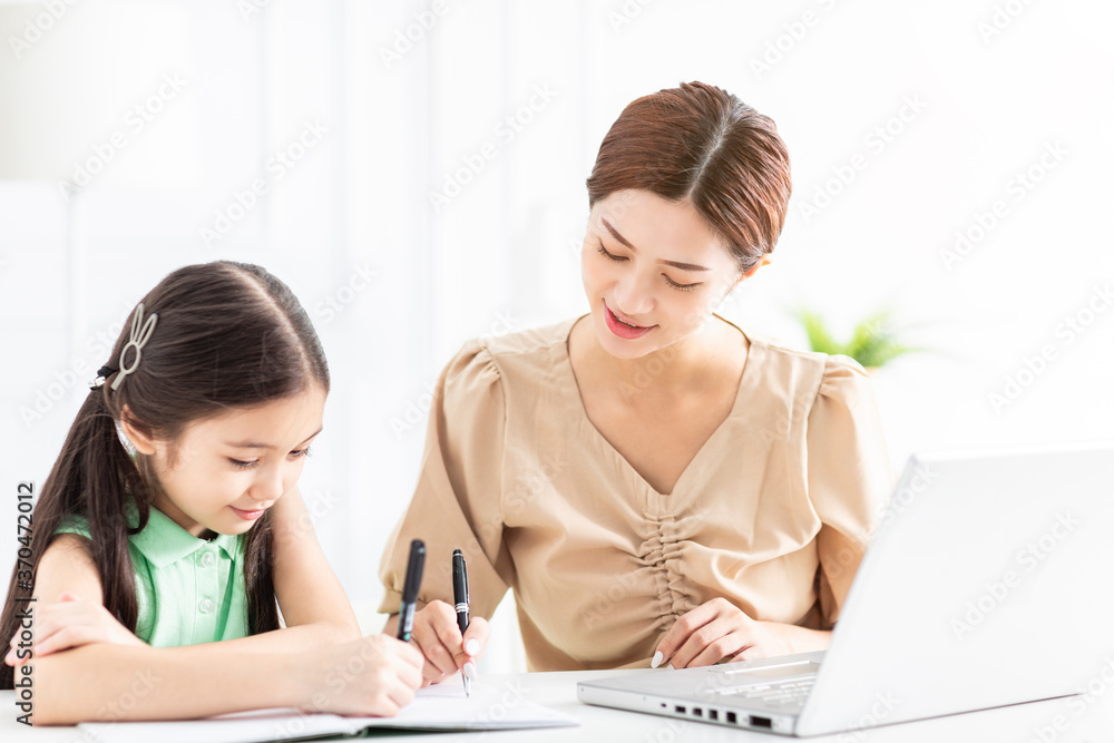 Mother is working and teaching her daughter doing home work Mother is working and teaching her daughter doing home work