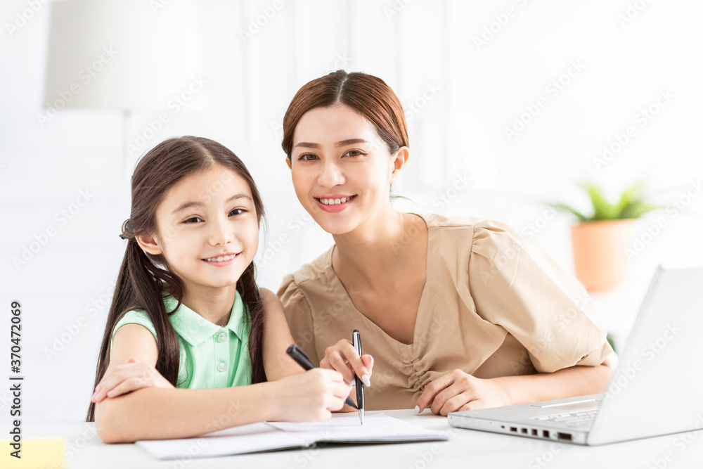 Fototapeta premium Mother is working and teaching her daughter doing home work