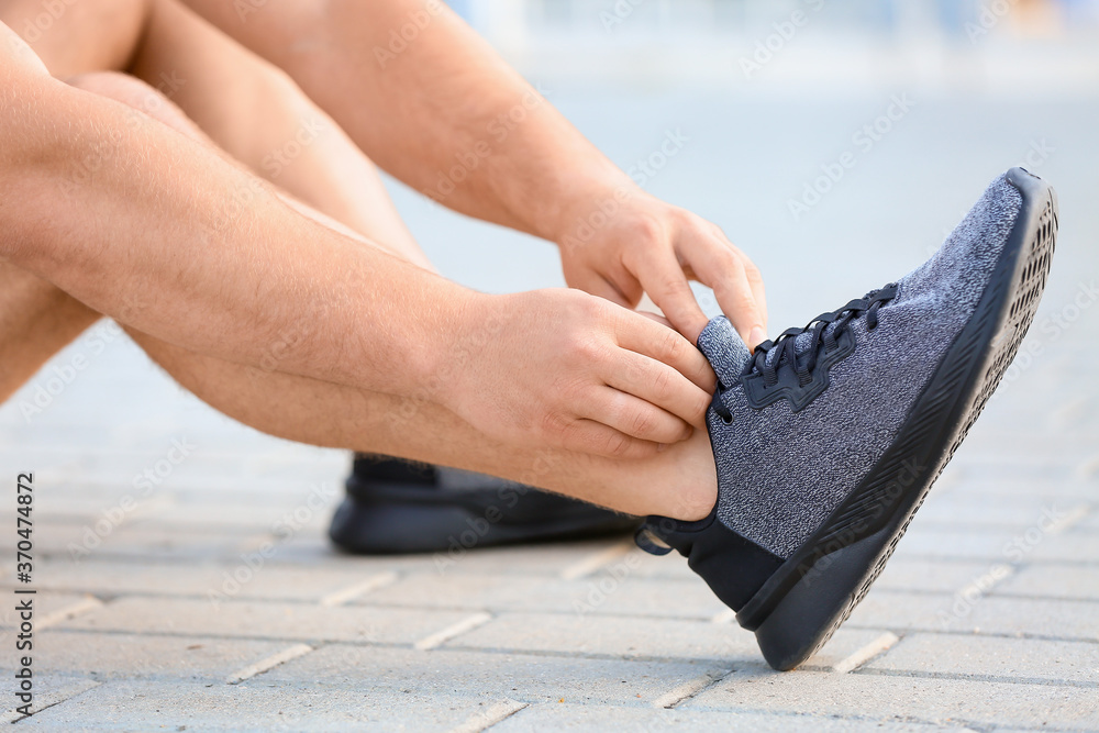 Sporty young man tying shoelaces outdoors, closeup - obrazy, fototapety, plakaty 