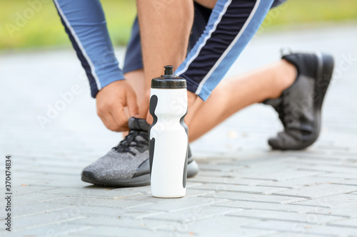 Bottle of water and sporty young man tying shoelaces outdoors, closeup