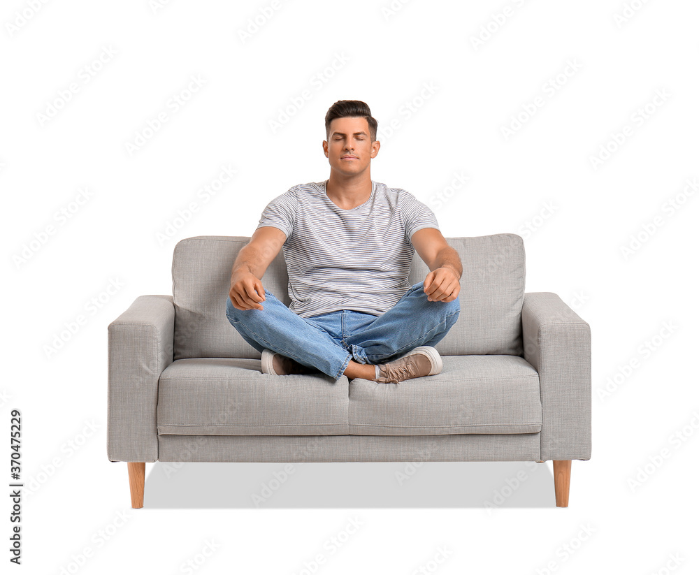 Young man meditating on sofa against white background