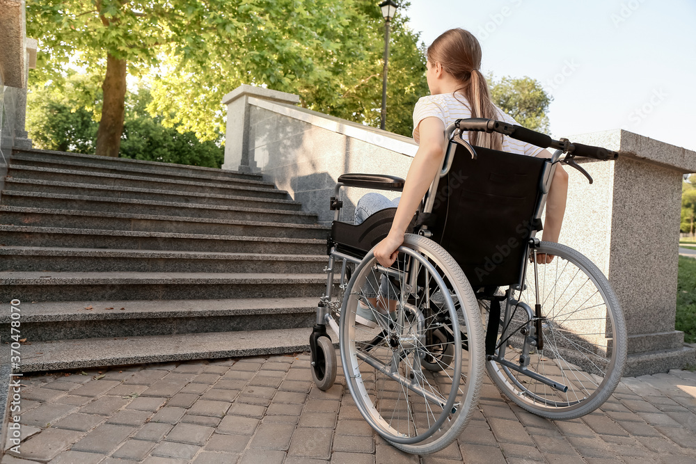Naklejka premium Young woman in wheelchair near stairs outdoors