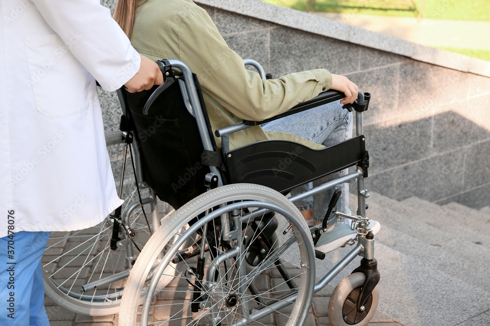Doctor and young man in wheelchair near stairs outdoors Doctor and young man in wheelchair near stairs outdoors