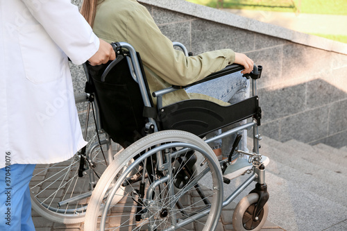 Doctor and young man in wheelchair near stairs outdoors