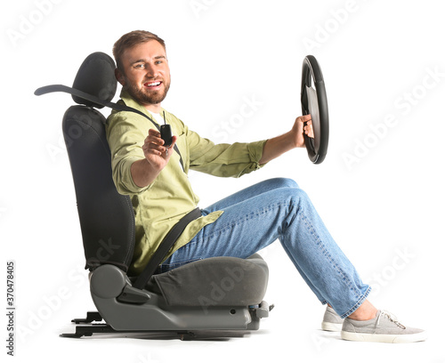 Young man with steering wheel and key sitting on car seat against white background photo