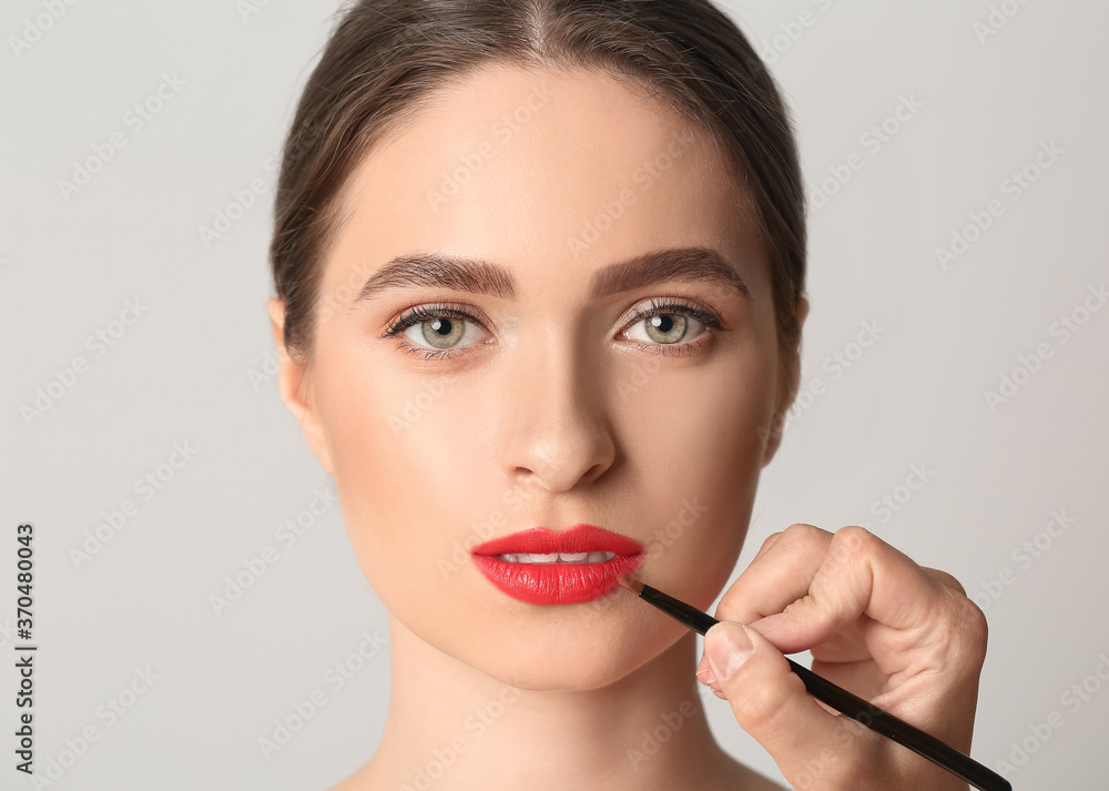 Makeup artist working with beautiful young woman on light background Makeup artist working with beautiful young woman on light background