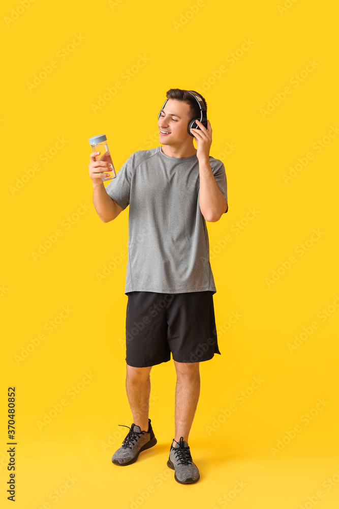Sporty young man with bottle of water and headphones on color background Sporty young man with bottle of water and headphones on color background