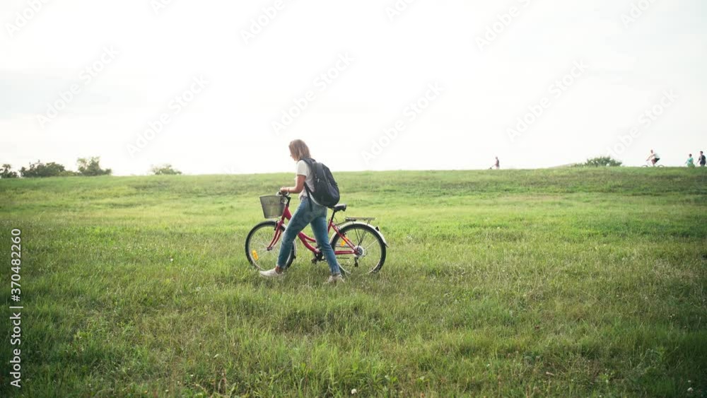 Cinematic shot of a young woman walking on a green field with a bicycle on sunset time. Cinematic shot of a young woman walking on a green field with a bicycle on sunset time.