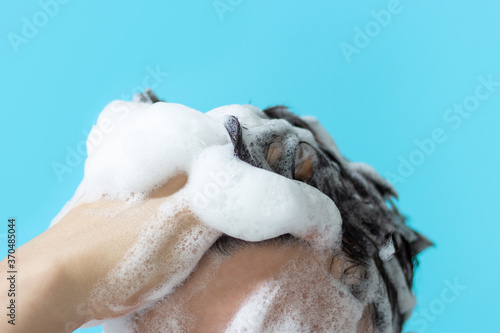 A man washes his hair with shampoo on blue background, copy of the space