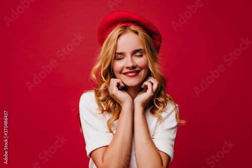 Beautiful european girl in french beret smiling in studio. Portrait of blissful blonde lady in good mood.
