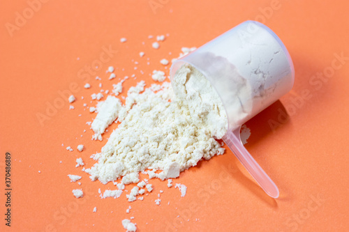 Measuring spoon with scattered protein powder, side view on a orange background photo