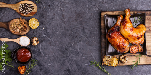 Rosemary baked chicken served on a black plate with lemon sauce tomato garlic and spices placed on a black table Top view and there is a blank space for designing the text.