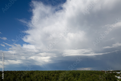 A big white cloud in a blue sky over a green forest