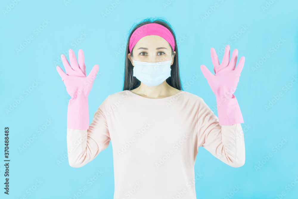 Young Asian Woman housewife in pink gloves wore face mask isolated on blue background,housework and household concept. Young Asian Woman housewife in pink gloves wore face mask isolated on blue background,housework and household concept.