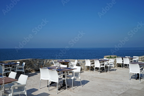 Exterior restaurant architecture and hotel dining area decoration decorated with white wooden furniture and palm tree with natural landscape view of ocean sea and clear blue sky © chettarin