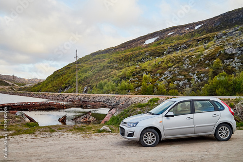 Fototapeta Naklejka Na Ścianę i Meble -  Small car standing on the side of road near wate of lake, river, fiord, sea and ocean.