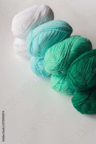 acrylic soft pastel green, azure and white colored wool yarn thread skeins row on white background, top angle view, vertical stock photo image with copy space for text