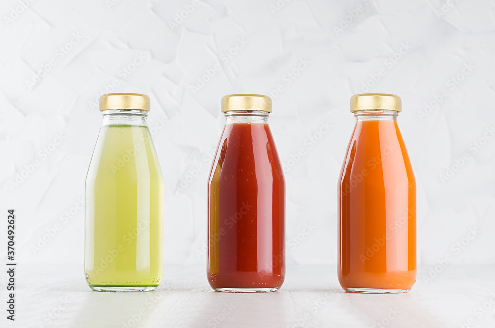 Tomato, carrot, green vegetable juices set in glass bottles with cap mock up in row on white wood table in light interior, template for packaging, advertising, design product, branding. Tomato, carrot, green vegetable juices set in glass bottles with cap mock up in row on white wood table in light interior, template for packaging, advertising, design product, branding.