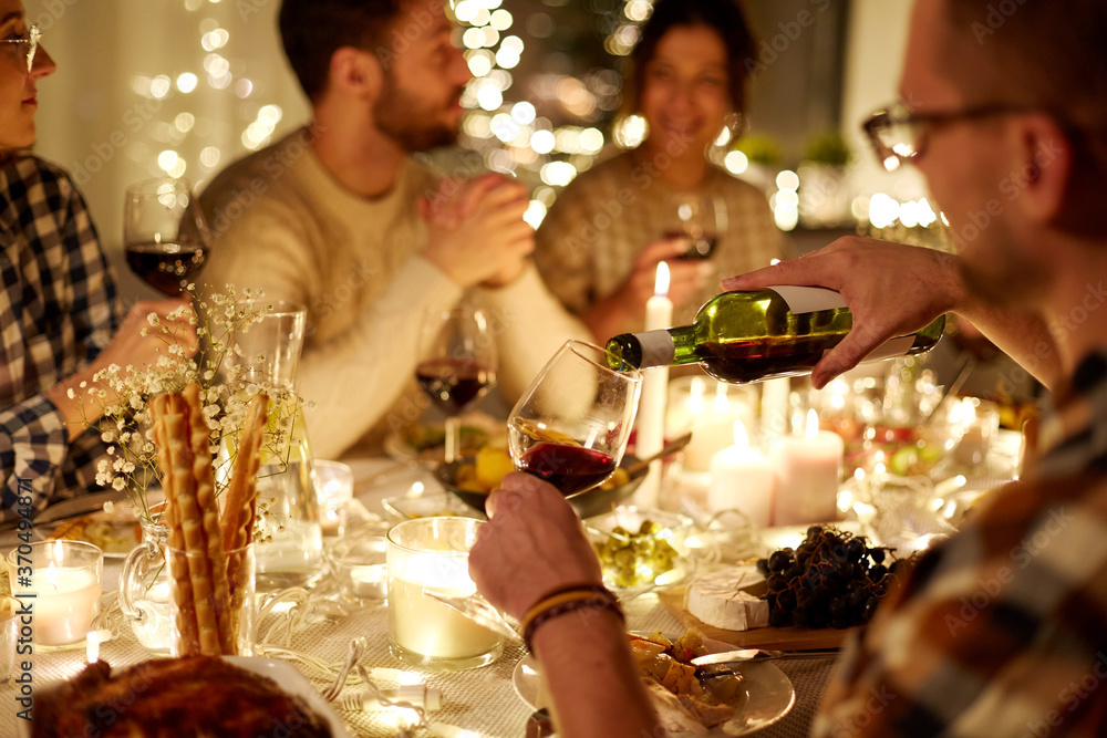 holidays and celebration concept - man pouring red wine into glass at christmas party