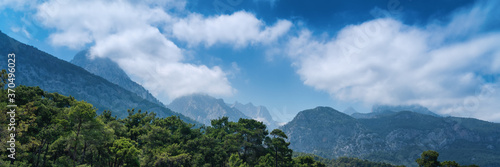 Beautiful mountain landscape, pine forest on hills with blue sky and clouds, panorama banner format