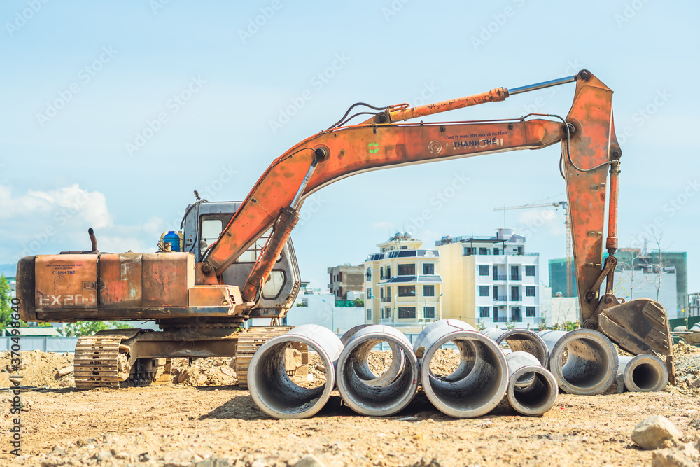 Stack of concrete drainage pipes for wells water discharges laying an external sewage system at a construction site and yellow digger excavator machine equipment. Civil building industry Stack of concrete drainage pipes for wells water discharges laying an external sewage system at a construction site and yellow digger excavator machine equipment. Civil building industry