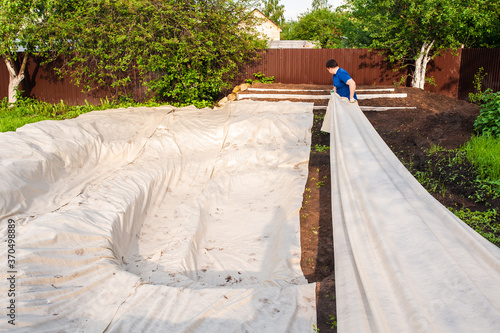 A man covers a dug hole with geotextile. Garden work, do-it-yourself pool