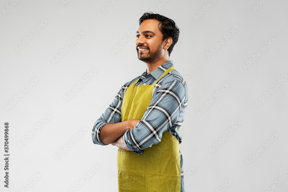 gardening, farming and people concept - happy smiling indian male gardener or farmer in apron with crossed arms over grey background gardening, farming and people concept - happy smiling indian male gardener or farmer in apron with crossed arms over grey background