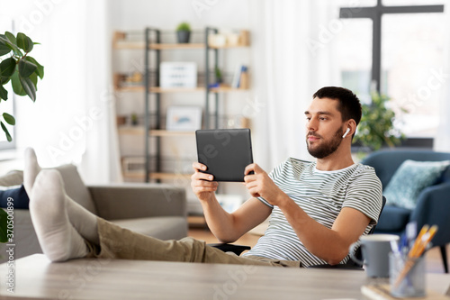 technology, remote job and lifestyle concept - man with tablet pc computer and earphones resting feet on table at home office