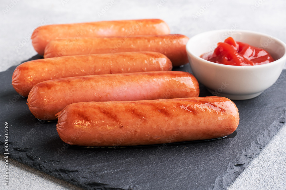 Juicy grilled meat sausages with tomato sauce and ketchup on a concrete stand. Fat fast food. Concept unhealthy eating. Juicy grilled meat sausages with tomato sauce and ketchup on a concrete stand. Fat fast food. Concept unhealthy eating.