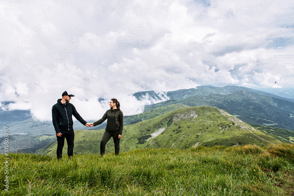 A couple in love walk holding hands on the top of mountain with a scenic view on the background
