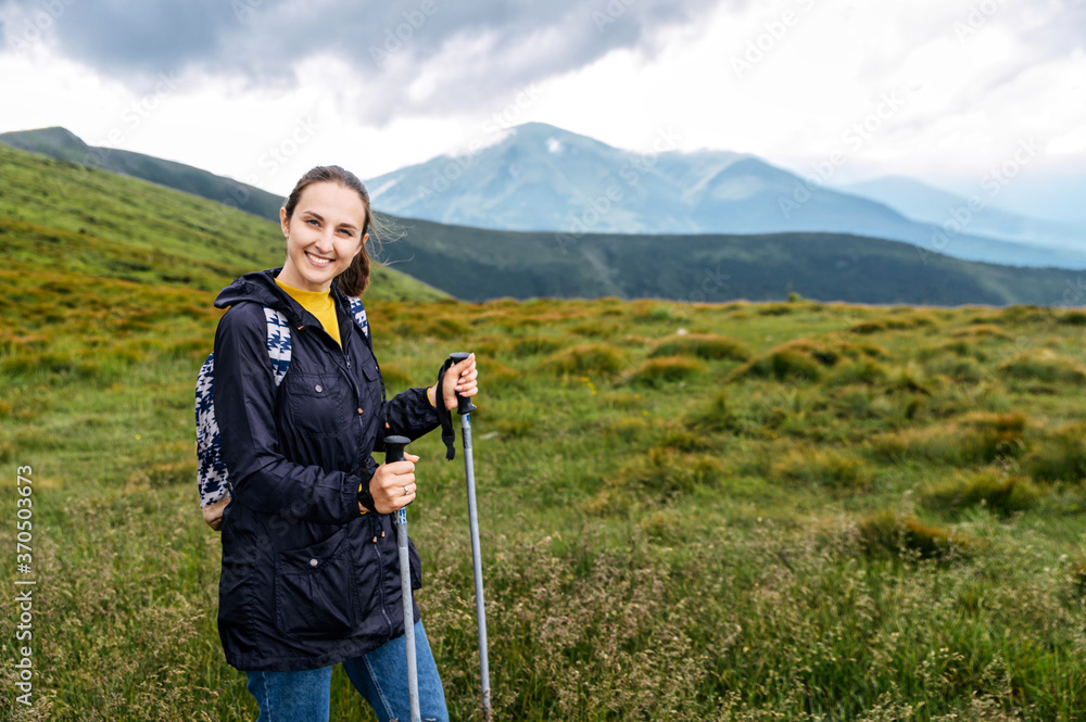 A young woman with hiking sticks outdoors on the mountains footpath. Camping, active vacation
