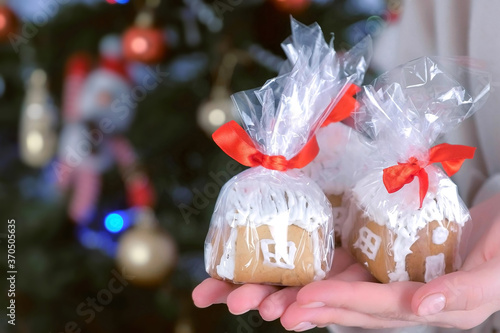 Gingerbread houses in package as presents for Christmas on woman's hands on tree background. New Year atmosphere at home. Preparing gifts for holiday. Sweet homemade bakery. photo