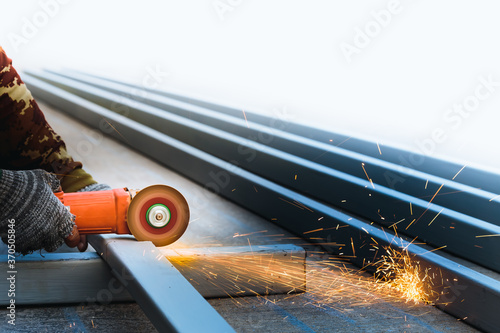A male worker wearing cloth gloves was cutting the metal with a circular disc electric grinder which rotated at high speed, causing an orange spark to spill onto the front steel pile.