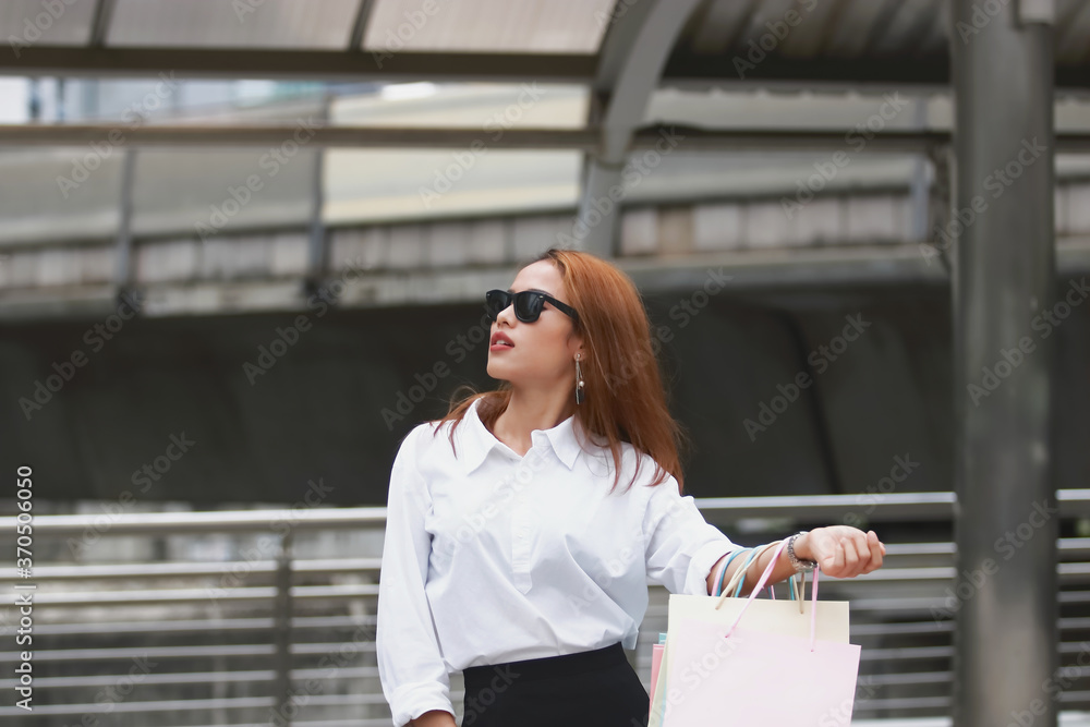 Portrait of attractive happy young Asian woman in casual clothes carrying colorful shopping bags outdoors