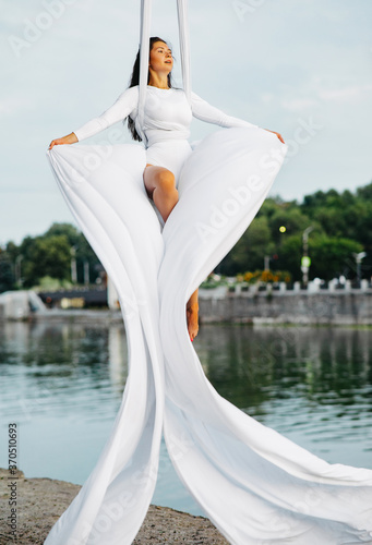 Woman aerialist performs acrobatic tricks on hanging aerial silk and waving by fabric. photo