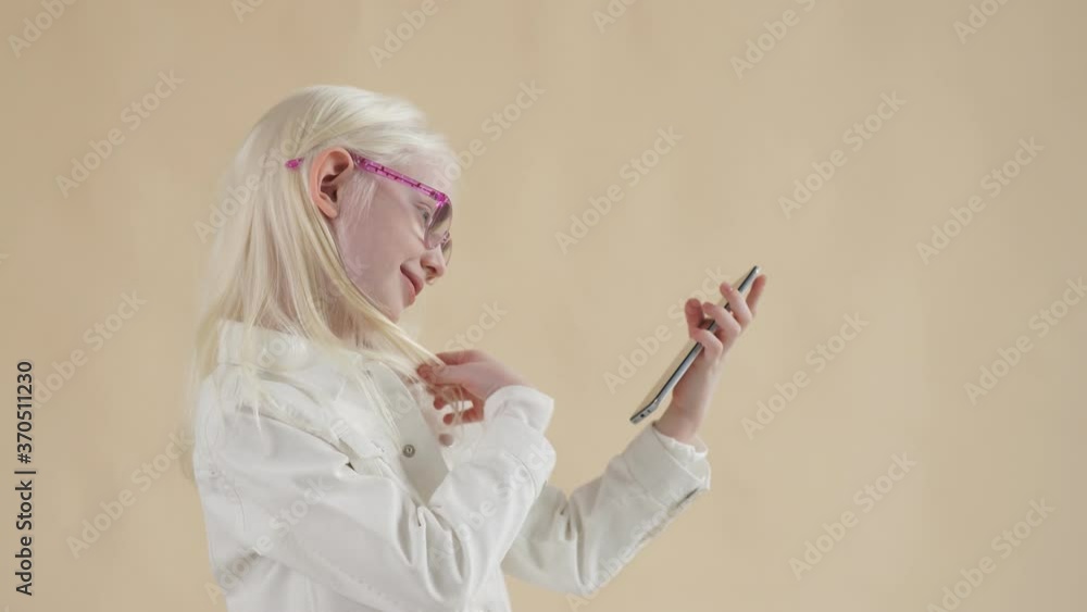Innocent unusual albino kid girl watching videos on smartphone, look at screen of mobile phone Innocent unusual albino kid girl watching videos on smartphone, look at screen of mobile phone